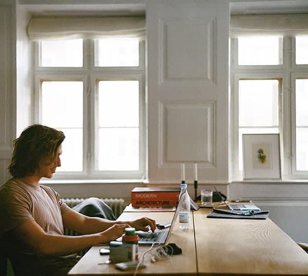 Freelancer working on a laptop sat on top of a wooden table in his family home