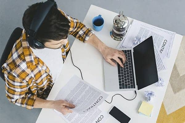 Birds eye view of freelancer holding a contract in one hand and typing on a macbook with the other hand.