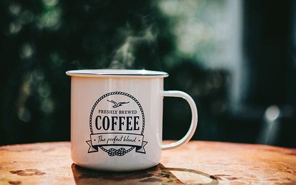 A white cup of steaming coffee placed on top of a wooden table