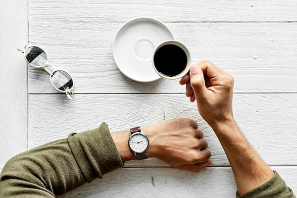 Birds eye view of a freelancer's hand holding an espresso coffee and other arm wearing a watch.