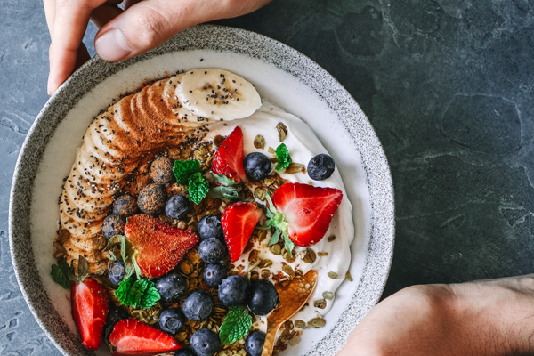 A healthy bowl of strawberries, seeds, muesli, mint leaves, blueberries, banana and cinnamon on a bed of yoghurt.