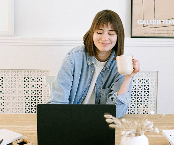 Lady smiling as she drinks a cup of tea and works from laptop