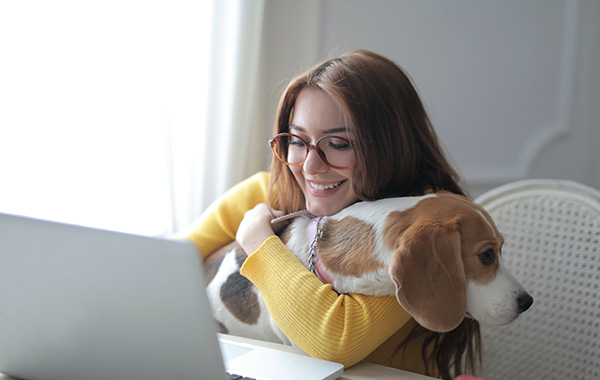 Lady working from home, hugging her dog as it sits on her lap.