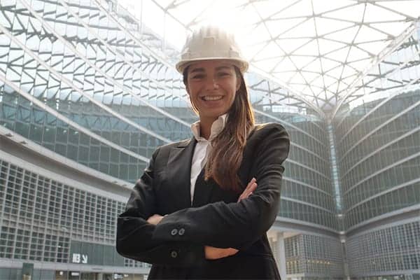 Female engineer in hard hat and suit, stood with arms folded smiling down at the camera