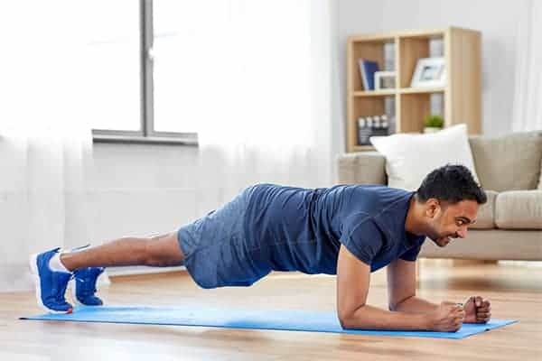 Man planking on exercise mat at home to get in daily exercise during lockdown.