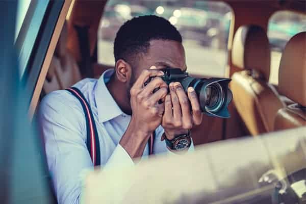 Wedding photographer sat in car holding camera close to face and capturing a picture.