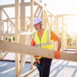 a tradesperson carrying a large piece of wood on a construction site