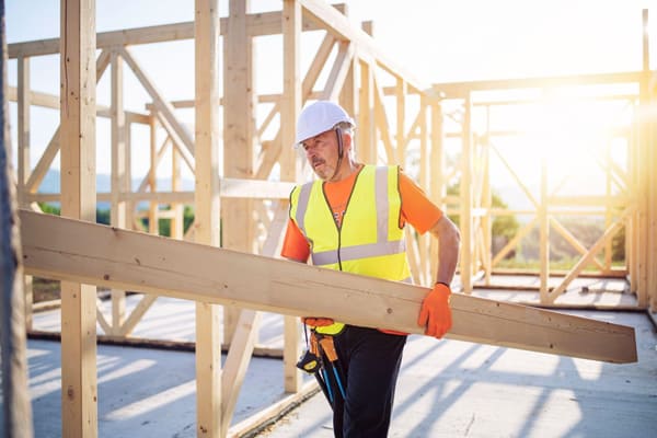 a tradesperson carrying a large piece of wood on a construction site